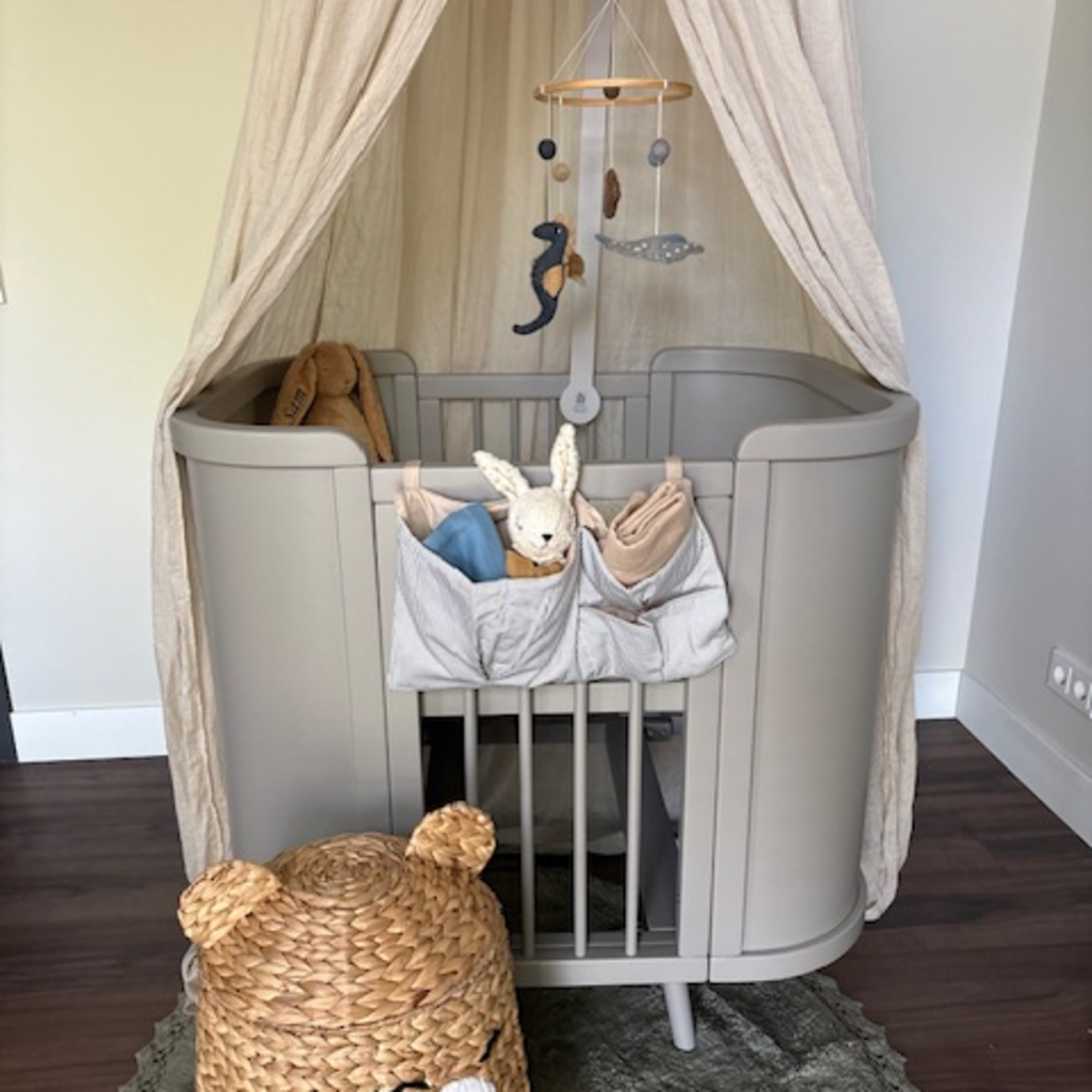 Beige meegroeibed van massief hout in een rustige babykamer met canopy en zachte accessoires