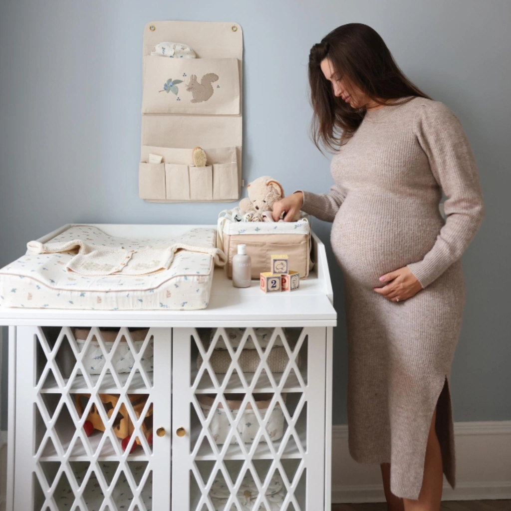 Zwangere vrouw bij rustig ingerichte Scandinavische babykamer met houten commode